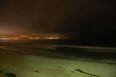 Illuminated beach against sky at night