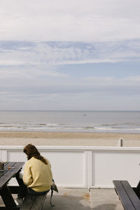 Rear view of woman sitting on beach against sky