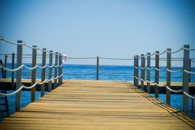 Pier over sea against clear blue sky