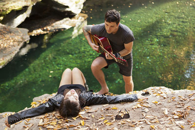 Young man serenading his girlfriend by a stream