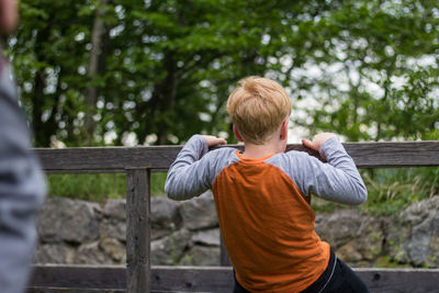 Rear view of boy playing on wooden fence at yard