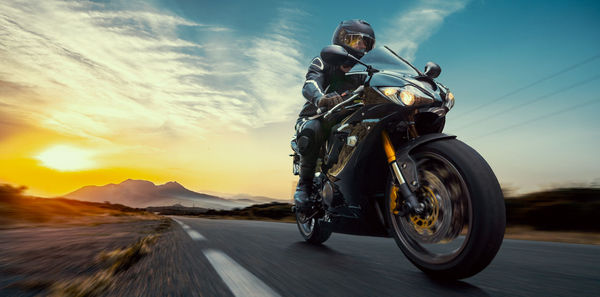 Man riding motorcycle on road against sky during sunset