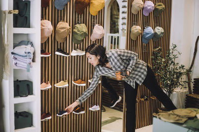 Saleswoman bending over while arranging shoes on display rack at fashion boutique