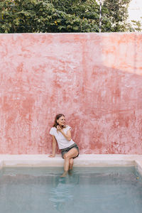 Portrait of young woman sitting crossed legged against a pink wall