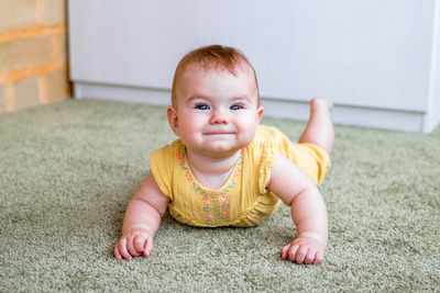 Portrait of smiling little caucasian baby girl in yellow dress. child trying to crawl on a floor.