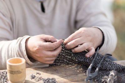 Midsection of man working on chain mail armor at table