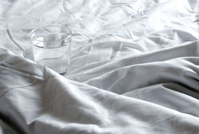 A glass of water on the blanket crumpled on the bed