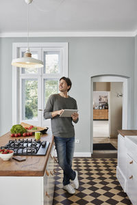 Man using tablet in kitchen looking at ceiling lamp
