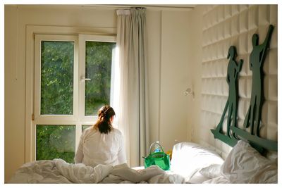 Rear view of woman sitting on bed at home