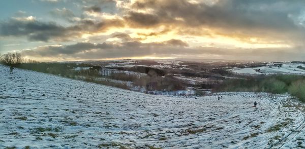 Snow covered land against sky during sunset