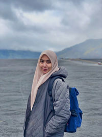 Portrait of young woman standing in sea against sky