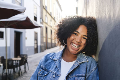 Happy woman with curly hair leaning on wall