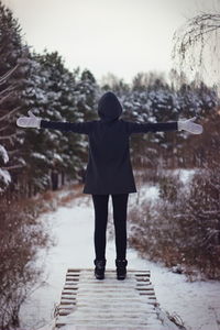 Rear view of woman with arms outstretched standing on footbridge against sky