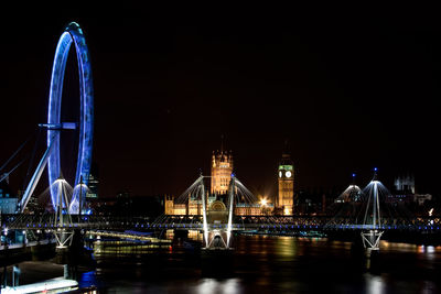 Illuminated bridge over thames river by millennium wheel in city against clear sky at night