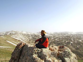 Man sitting on rock against mountain range against clear sky