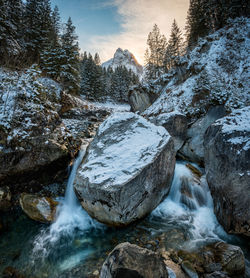 View of stream flowing through rocks during winter