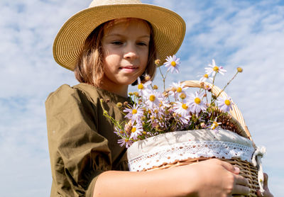 Girl in linen dress and a straw hat stands with a basket of daisies.
wellness and freedom concept.