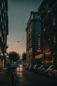 Illuminated city street and buildings against sky at dusk