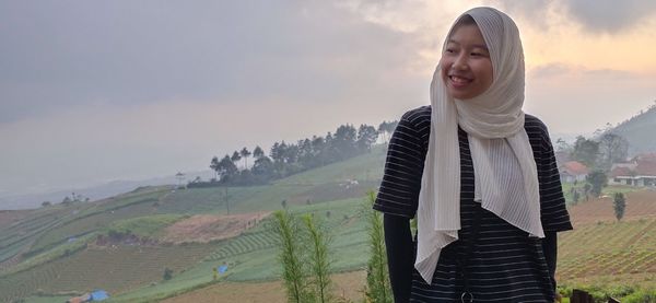 Smiling young woman standing against sky