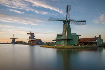 Traditional windmill by water against sky during sunset