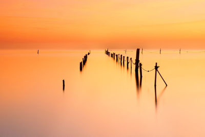Silhouette of wooden post in sea during sunset