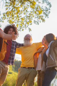 Group of people of different generations hugging each other in circle of friends lake at golden hour