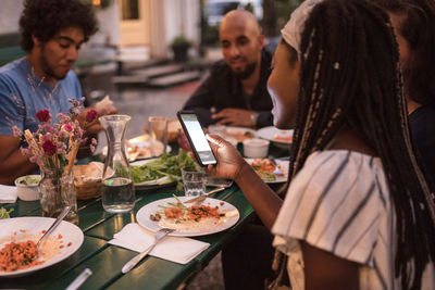 Young woman using smart phone while having dinner with friends during garden party