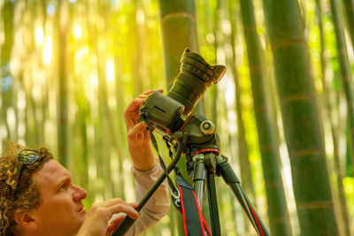 Man holding camera while standing amidst forest