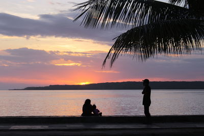 Silhouette woman on shore against sky during sunset