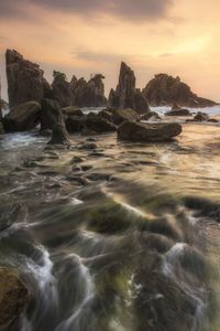 Rocks in sea against sky during sunset