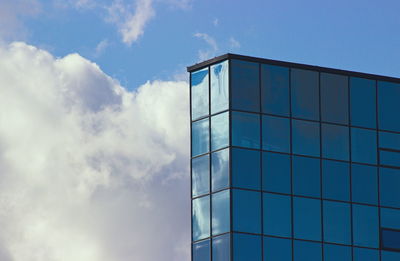 Low angle view of glass building against cloudy sky