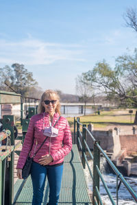 Portrait of cheerful adult woman with sunglasses standing on a footbridge