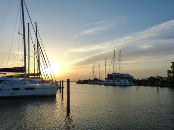 Boats moored in harbor at sunset