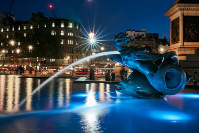 Illuminated buildings against blue sky at night