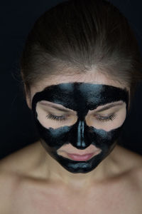 Close-up of young woman with facial mask against black background