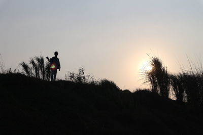 Silhouette man standing on field against sky during sunset