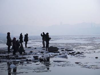 People at beach against clear sky during winter