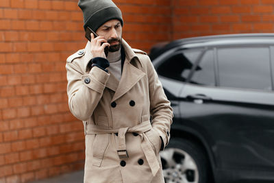 Close-up of a young, smiling, happy, laughing hipster with a beard in a raincoat and hat