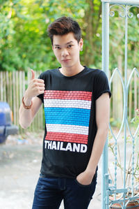 Portrait of young man gesturing thumbs up while standing outdoors