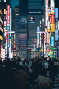 People walking on illuminated street amidst buildings in city at night