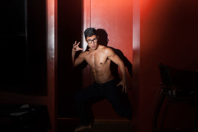 Portrait of shirtless muscular young man standing against red wall