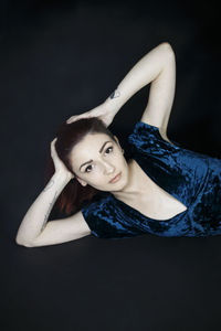 Portrait of beautiful young woman with hand in hair against black background