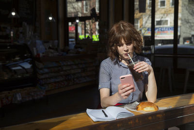 Woman drinking cola while using smart phone in cafe