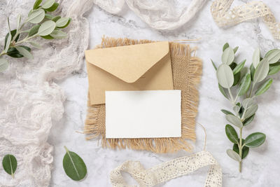 Blank card with envelope laying on a marble table decorated with eucalyptus branches 