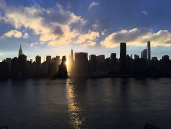 Modern buildings in front of river against cloudy sky during sunset