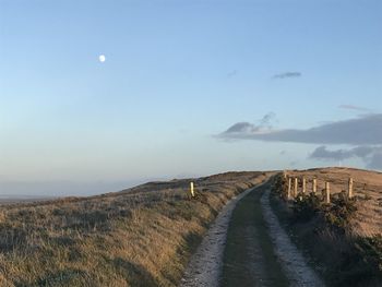 Empty road amidst field against sky