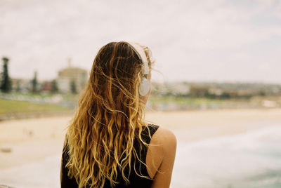 Rear view of woman listening to music against sky