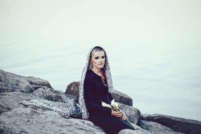 Woman looking away while sitting on rock at beach