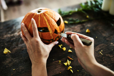 Cropped image of hand holding pumpkin against wooden table during halloween