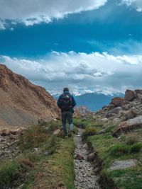 Rear view of young woman with backpack walking on mountain against cloudy sky